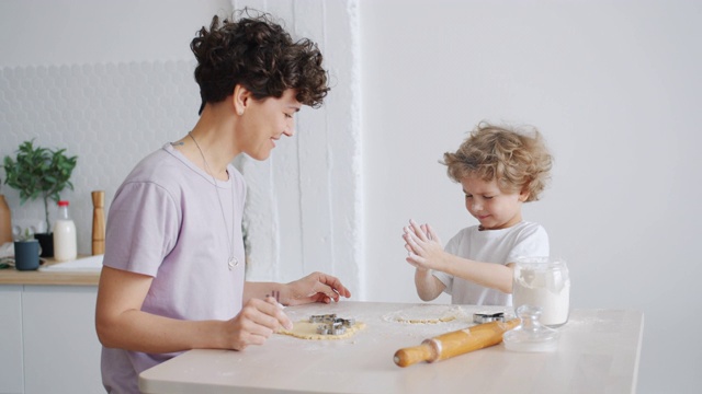 可爱的孩子拍着沾满面粉的手和妈妈在厨房做饼干视频素材