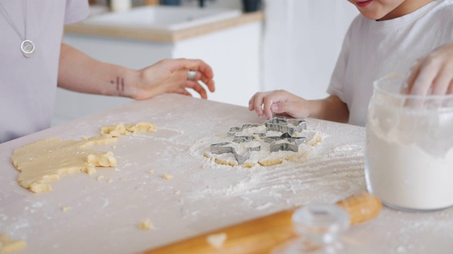 在厨房的桌子上，孩子帮助妈妈用面团和面粉做饼干视频素材