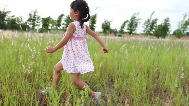 亚洲女童奔跑和欢笑在草地在夏天的自然视频素材