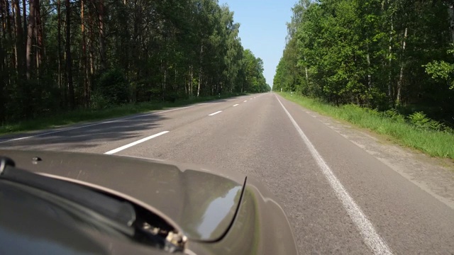 汽车沿着绿色的森林沿着道路行驶，你可以看到引擎盖。4 k缓慢莫视频素材