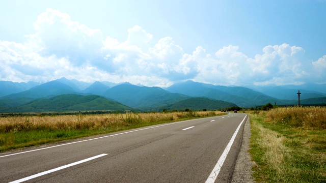 在阳光明媚的夏日，汽车行驶在通往远处山区的道路上视频素材