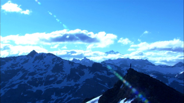 灿烂的阳光洒在雪山的山峰上，一个孤独的徒步旅行者站在那里。视频素材