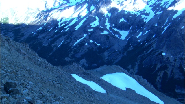 徒步旅行者穿过白雪覆盖的山脉下的山脊。视频素材