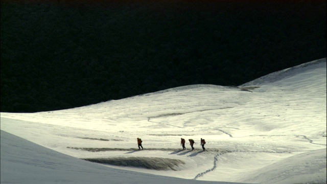 登山者在山脚下的雪地里行走。视频素材