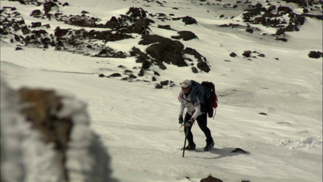 疲惫的徒步旅行者艰难地爬上白雪覆盖的斜坡。视频素材