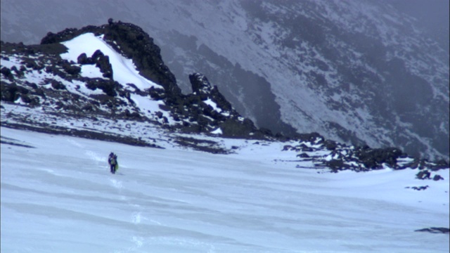 徒步旅行者走在白雪覆盖的山坡上。视频素材