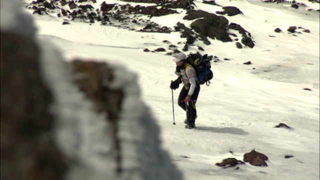 疲惫的徒步旅行者艰难地爬上白雪覆盖的斜坡。视频素材