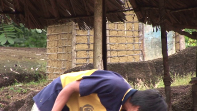 一个土著人在一间小屋前捡起了什么东西。视频素材