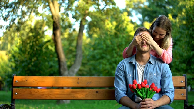 女孩闭上男友的眼睛，带着一束鲜花在公园等她，惊喜视频素材