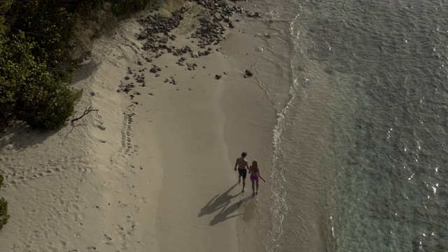 航拍镜头，一对夫妇在格林纳达卡里亚库海滩/安斯拉罗希湾(Anse La Roche bay)手拉手散步视频素材