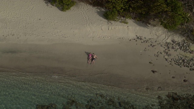 远处的夫妇坐在海边附近的海浪/安斯拉罗希湾，卡里亚库，格林纳达鸟瞰图视频素材