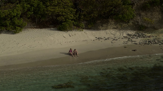 空中放大，一对夫妇坐在海滩附近的海浪/ Anse La Roche湾，卡里亚库，格林纳达视频素材