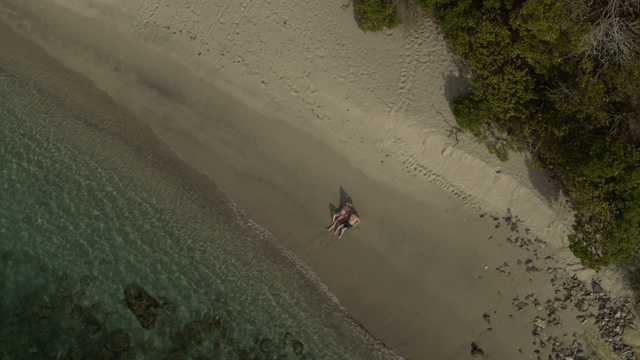 镜头从一对夫妇坐在海滩附近的海浪/ Anse La Roche湾，卡里亚库，格林纳达视频素材