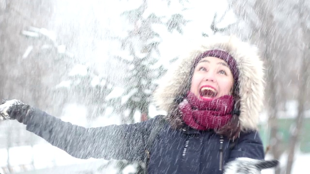 美丽的年轻女孩用手抛出雪花，积极地表达她的喜悦，大笑和拍手。视频素材