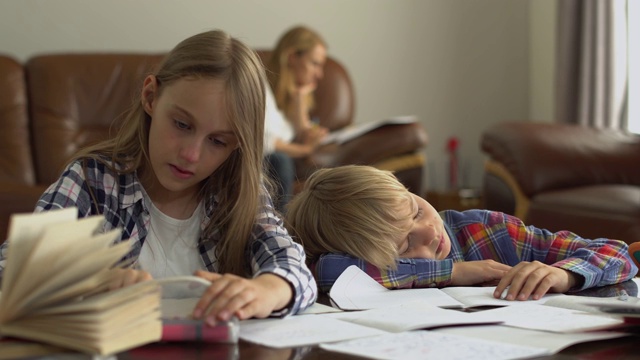 两个可爱的小学生在家里学习，他们的母亲坐在后面。视频素材