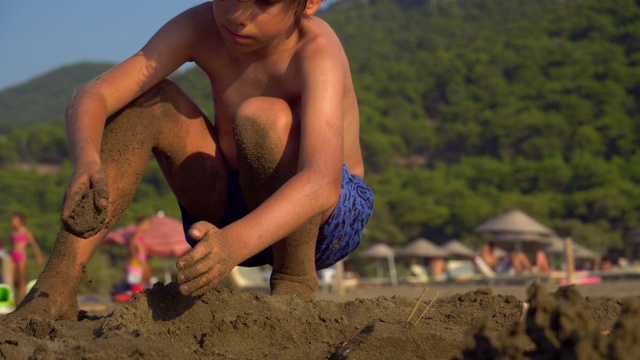 一个男孩在土耳其穆格拉的伊兹图祖海滩上做沙堡。视频素材