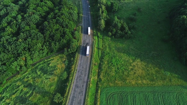 空中飞过沿着绿色山谷包围的道路行驶的卡车。4 k。视频素材