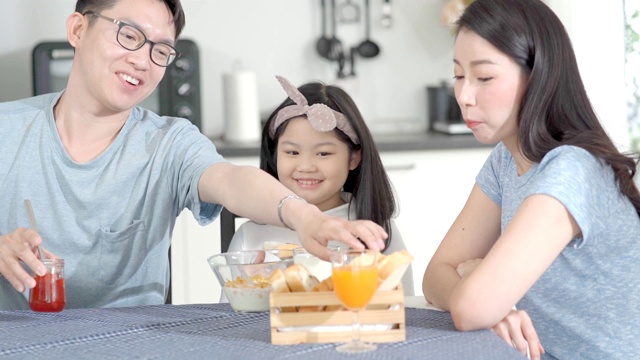 父母和女儿吃麦片牛奶早餐早上在厨房。视频素材