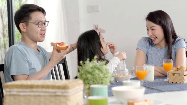 父母和女儿吃麦片牛奶早餐早上在厨房。视频素材