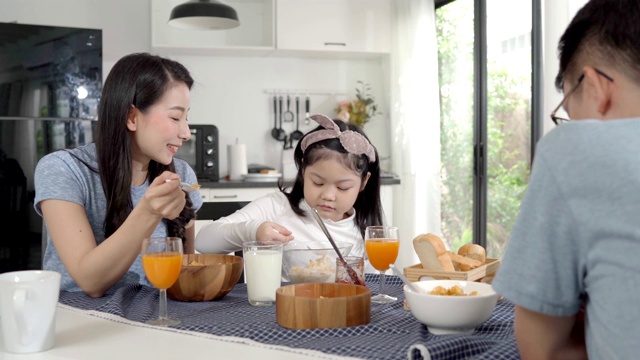 父母和女儿吃麦片牛奶早餐早上在厨房。视频素材