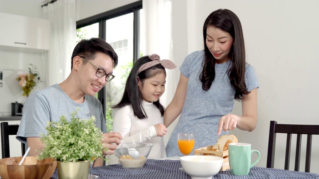 父母和女儿吃麦片牛奶早餐早上在厨房。视频素材