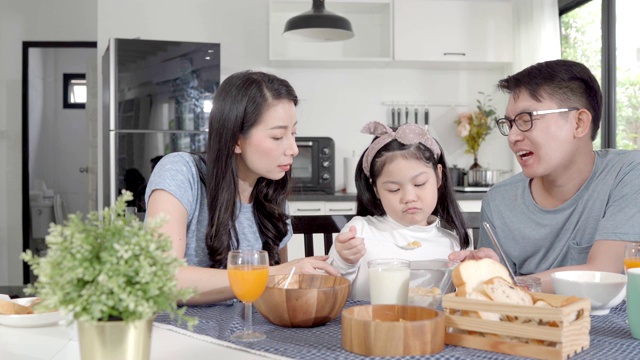 父母和女儿吃麦片牛奶早餐早上在厨房。视频素材