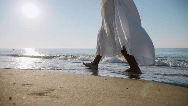 穿着白色裙子的女孩赤脚走在海边的海浪上视频素材