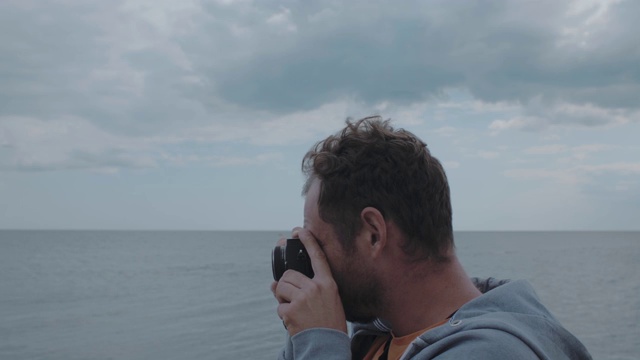 一名摄影师的肖像，一个男人的胡子谁拍摄的大海看取景器。4 k。4 k的视频。30帧视频素材