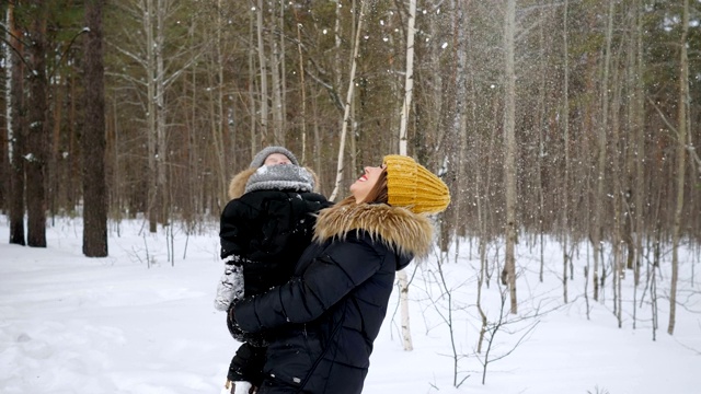 一位年轻的妈妈手里抱着小儿子，正在冬天的森林里看雪。视频素材