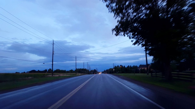 开车穿过乡村接近城市的地平线上的灯光。Driving Point of View POV Driving Towards into Urban Limits in Day。视频素材