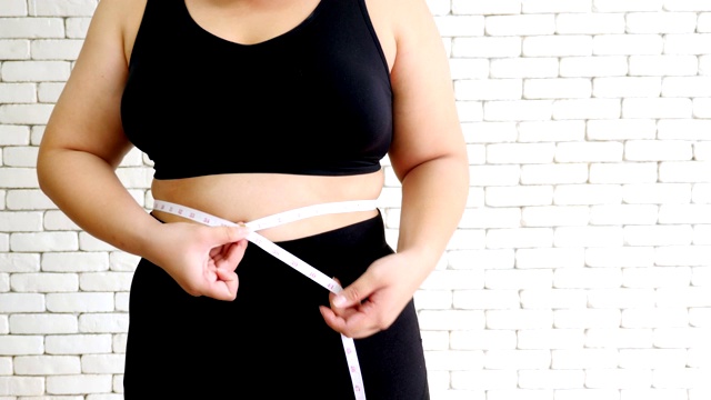 不快乐的超重妇女穿着运动服用卷尺测量腰围视频素材
