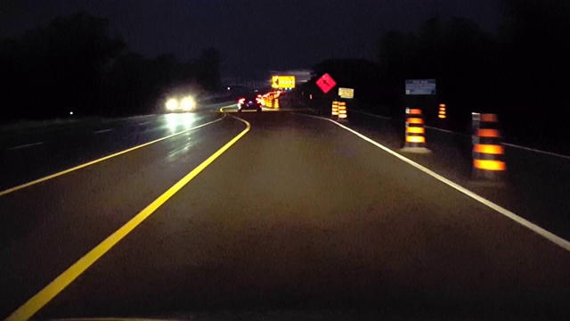 乡郊道路的行车巷终了，夜间有建筑路标。司机观点POV橙色警告道路标志，当驾驶乡村街道在晚上。视频素材