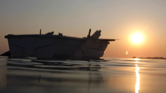 在日落时，漂浮在公海上的空的旧木船视频素材