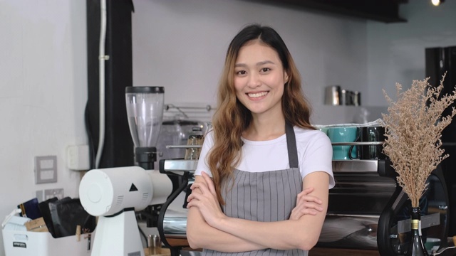 亚洲女性咖啡师小企业主手臂交叉微笑和看着相机在柜台酒吧在咖啡店。开创年轻人的事业。慢动作视频素材