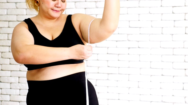 不快乐的超重妇女穿着运动服，用卷尺测量手臂视频素材