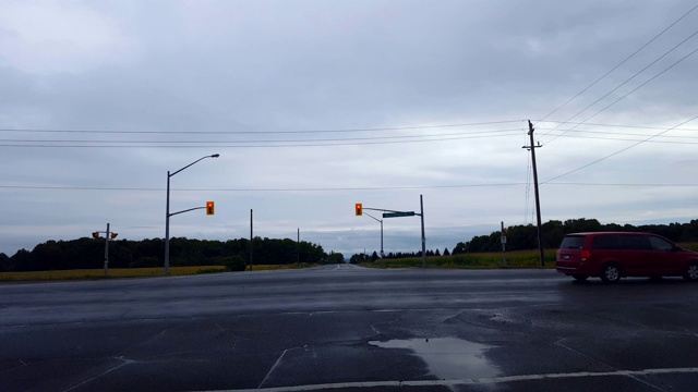 司机视角:在阴天下的乡村道路上等待红灯。交通通过车辆等待绿灯时的汽车。视频素材