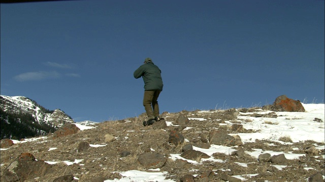 一个徒步旅行者爬上一个满是积雪的岩石斜坡。视频素材