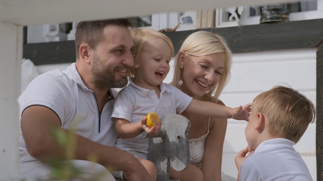 快乐的四口之家，孩子们在门廊上玩耍。妈妈，爸爸和两个儿子视频素材