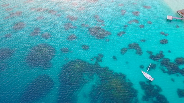 黄昏时分，在美丽的热带海滩上，空中俯瞰着风景如画的水上小屋，无人机向前飞行，同时倾斜并下降，越过水面——波拉波拉，法属波利尼西亚视频素材