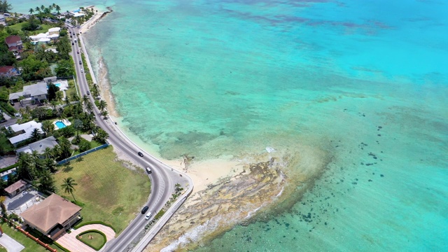 航拍:在巴哈马群岛拿骚清澈热带水域旁的风景优美的道路上行驶的汽车视频素材