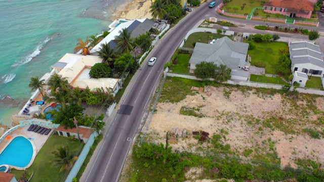 航拍:一辆白色汽车沿着海滨道路行驶，经过巴哈马群岛拿骚的热带海滨住宅视频素材