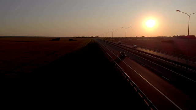 许多汽车是移动的夕阳。空中拍摄的车辆在美丽的乡村道路在日落。鸟瞰道路上的汽车与日落的背景。视频素材