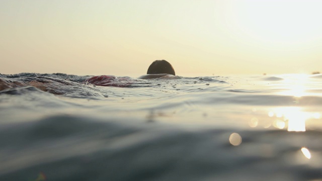 夕阳西下，一个年轻人在海里游泳视频素材