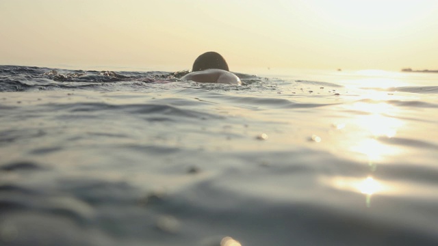 夕阳西下，一个年轻人在海里游泳视频素材