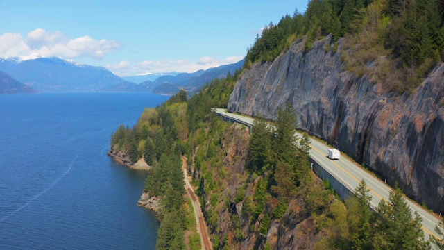 航拍:露营车在高速公路上翻越山脉的峡湾，车辆在道路上的树木在阳光明媚的日子-狮子湾，不列颠哥伦比亚省视频素材