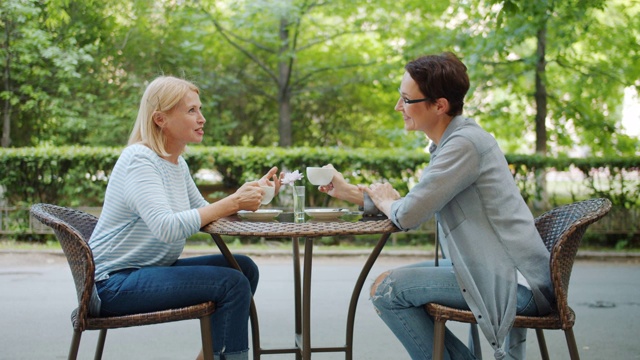 美丽的中年妇女拿着咖啡杯在户外咖啡馆聊天视频素材