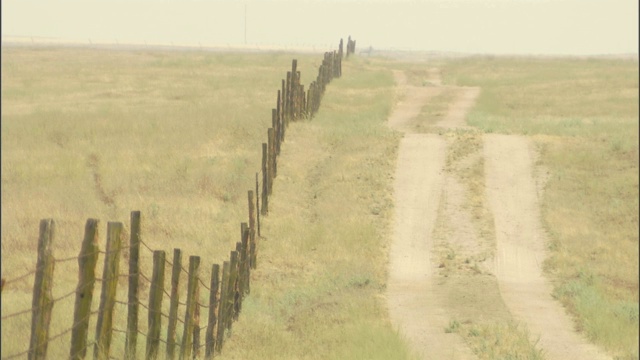 在农村地区，一条土路在农场栅栏的旁边。视频素材