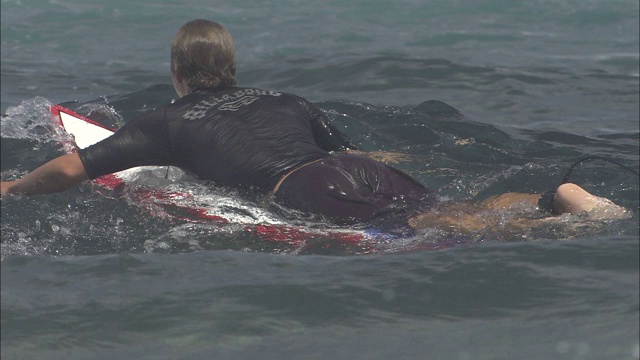 冲浪者用双臂划着冲浪板在波浪中滑行。视频素材