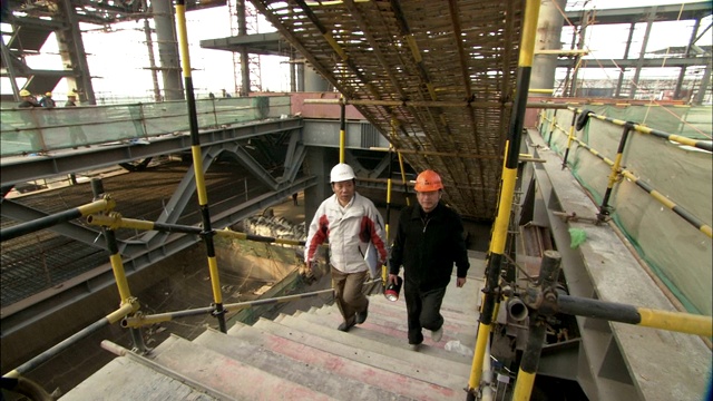 两名建筑工人在一个大型建筑工地上爬楼梯。视频素材