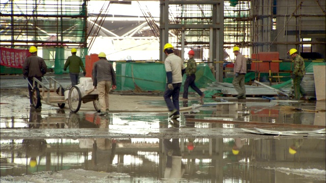 一个建筑工人推着一辆装满积木的手推车穿过建筑工地。视频素材